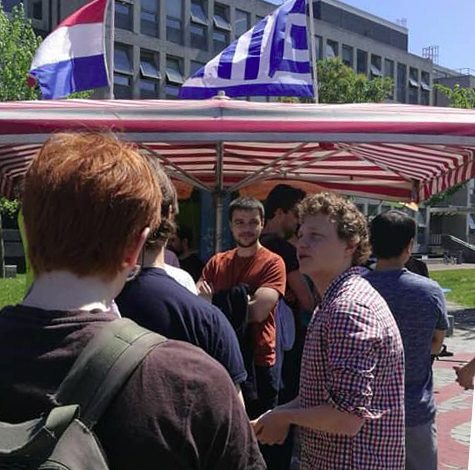 Een rij mensen voor de kraam onder Griekse en Nederlandse vlag